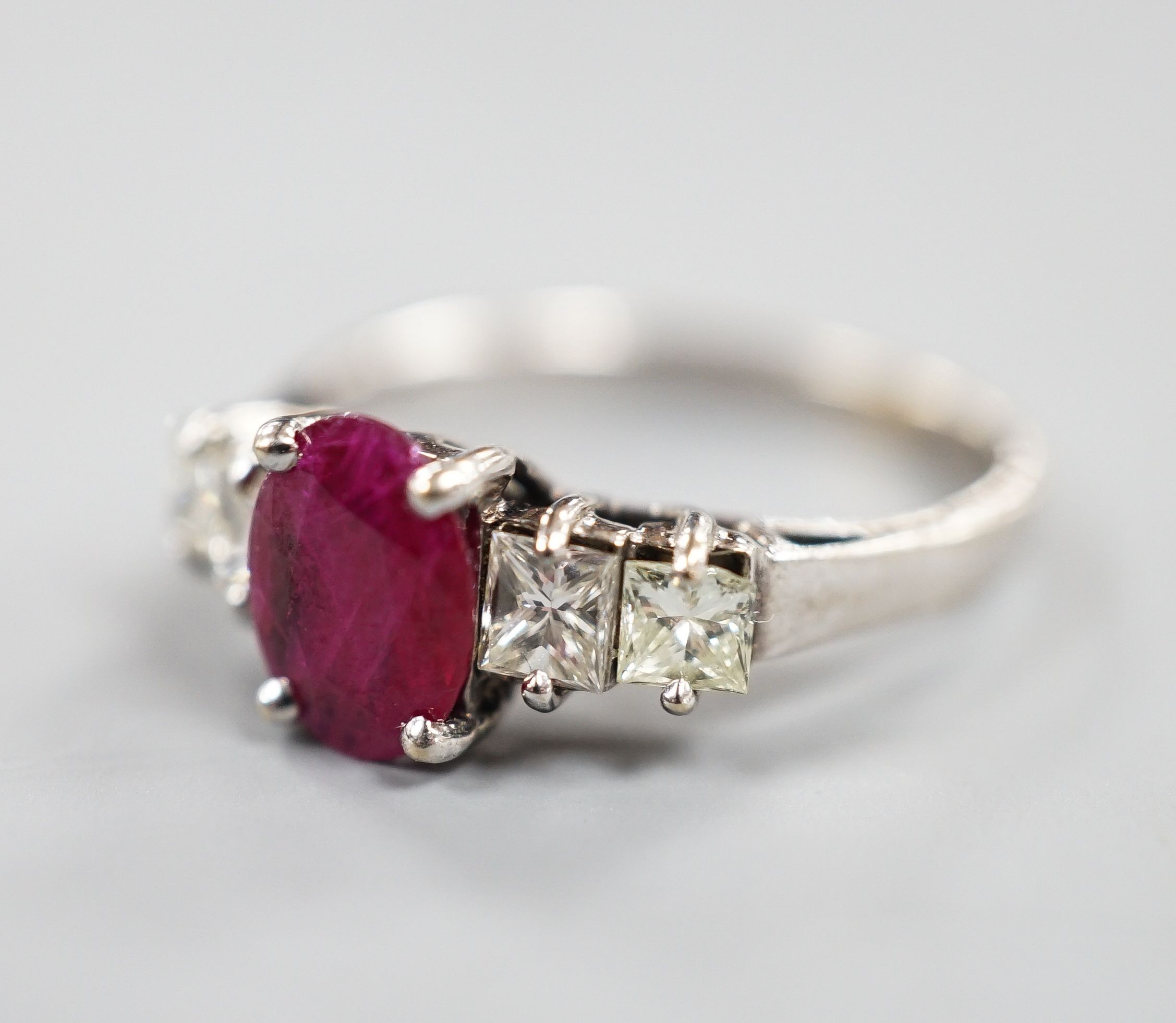 A modern 750 white metal single stone ruby and four stone princess cut diamond set half hoop ring, size M, gross weight 3.2 grams.